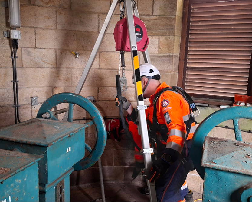 A technical rescue operative wearing high-visibility overalls and a helmet assisting with a Confined Space Rescue operation