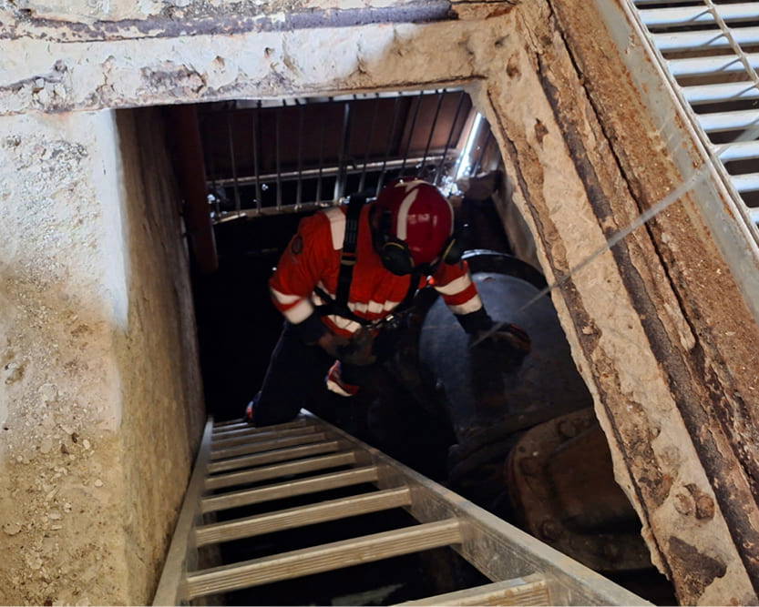 A AGO Fire & Rescue technical rescue operative wearing high-visibility overalls standing at the base of a ladder in a Confined Space