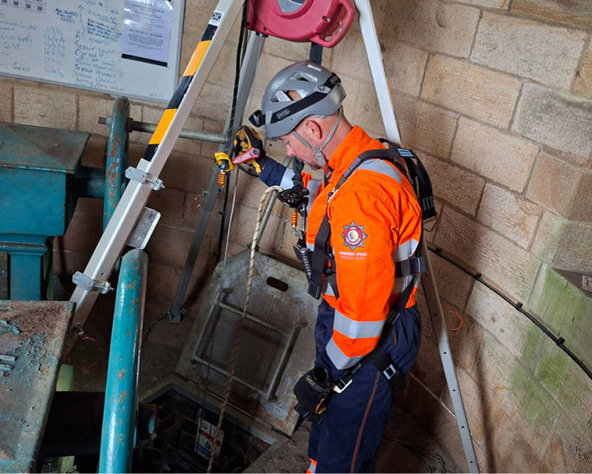 A technical rescue operative wearing high-visibility overalls assisting with a Confined Space Rescue operation in a small space